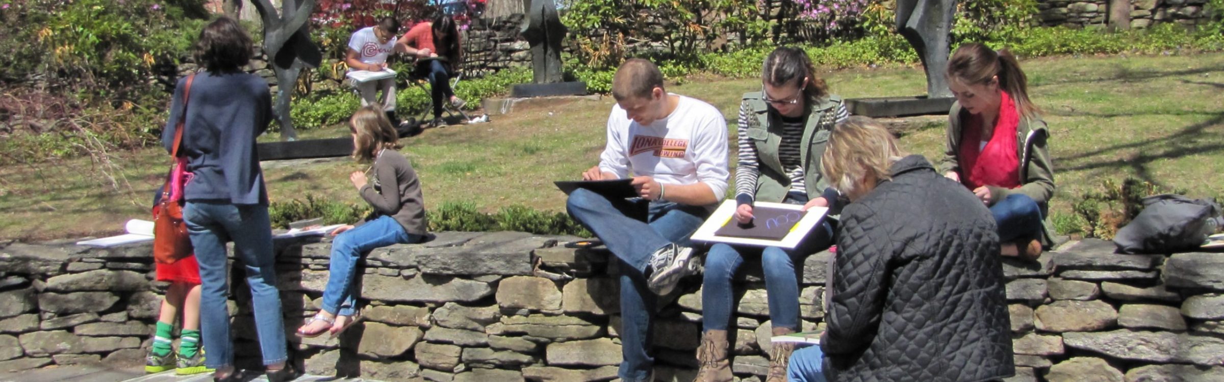 Image of families sitting on a stone wall and drawing together outside of The Benton Museum.